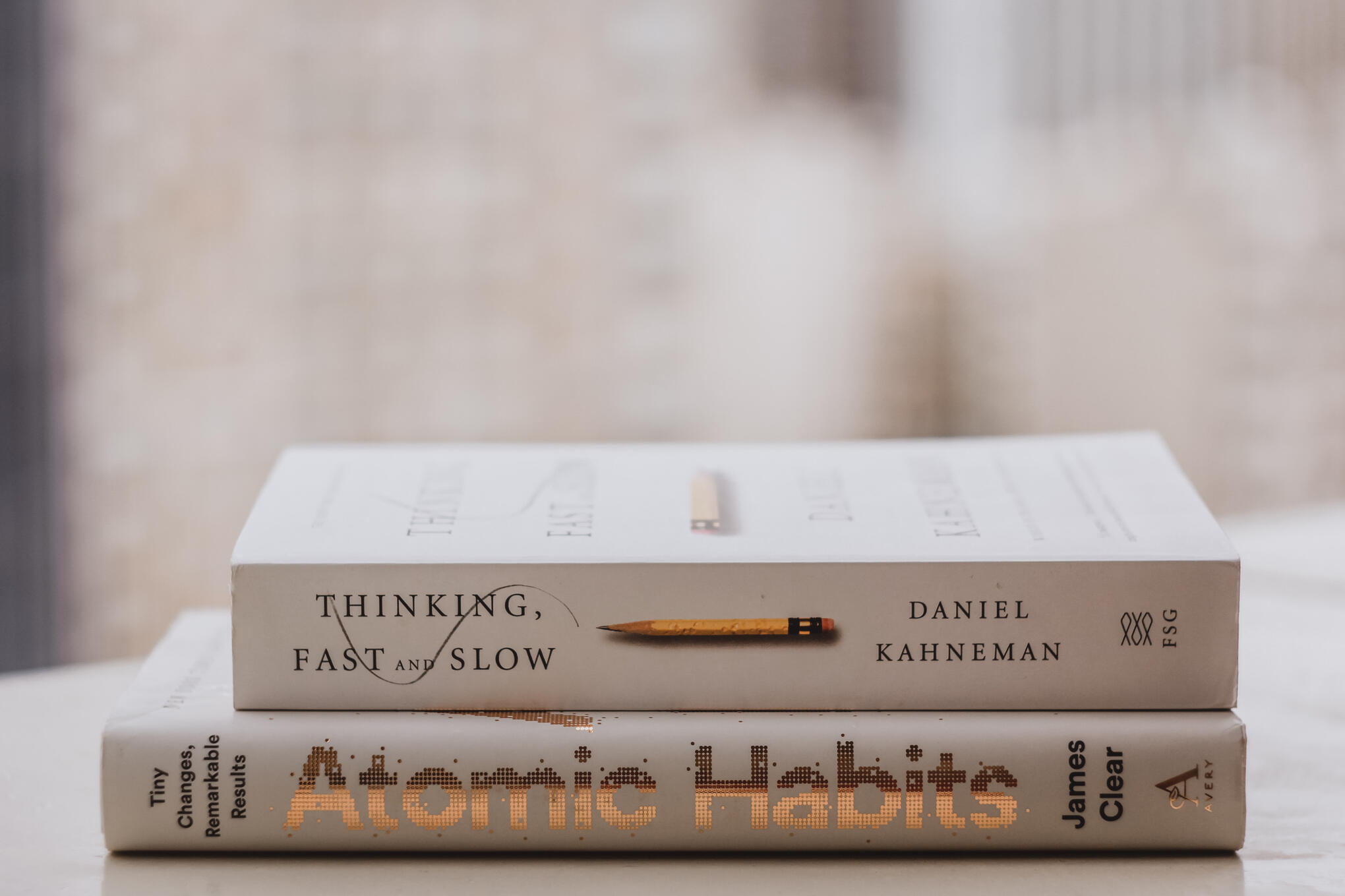 Photo of 2 stacked books, Atomic Habits by James Clear underneath Thinking, Fast and Slow by Daniel Kahneman by Lala Azizli on Unsplash
